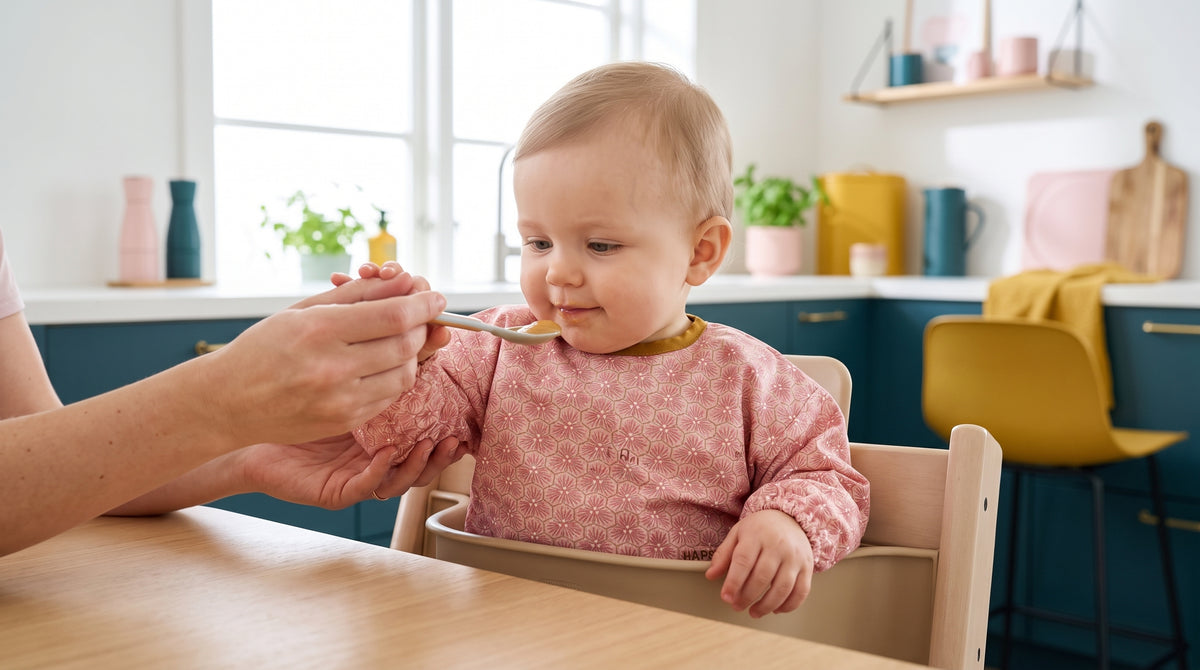 Baby im Hochstuhl mit rosa HAPSI Ärmellätzchen wird mit dem Löffel gefüttert