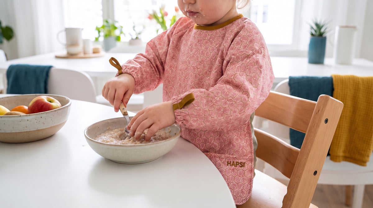 Kind mit rosa HAPSI Ärmellätzchen isst aus einer Schale