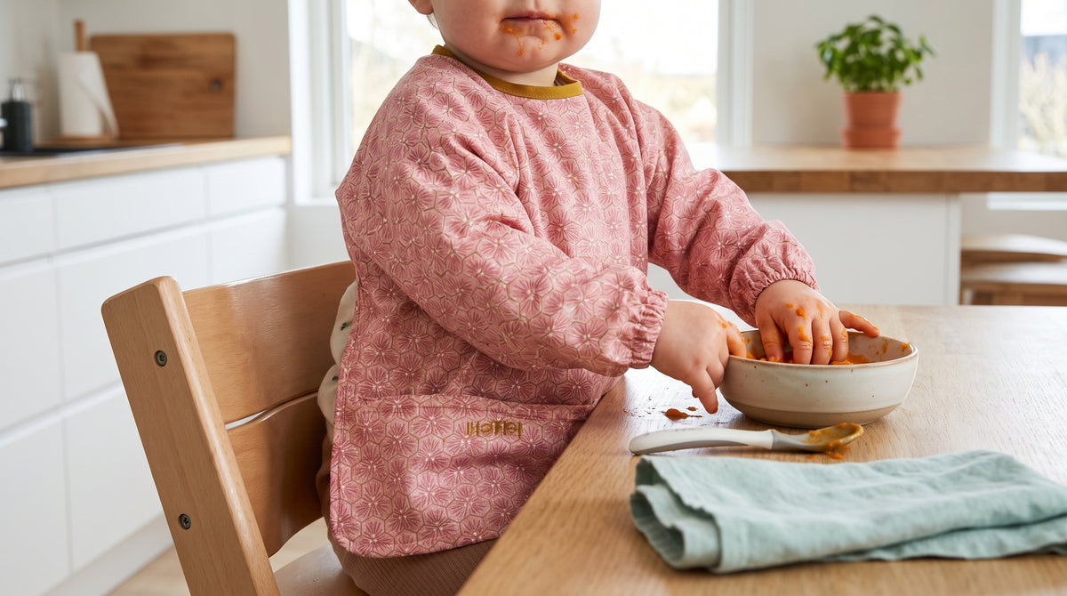 Kleinkind mit rosa HAPSI Ärmellätzchen isst am Tisch aus einer Schale