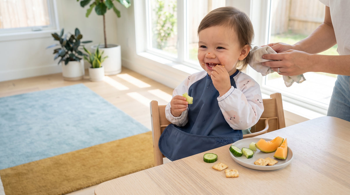 Lachendes Kleinkind mit blauem HAPSI Klecksi beim Essen